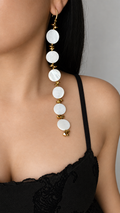 A close-up of a model wearing a long, dangling earring made of mother of pearl shell beads and gold plated glass beads