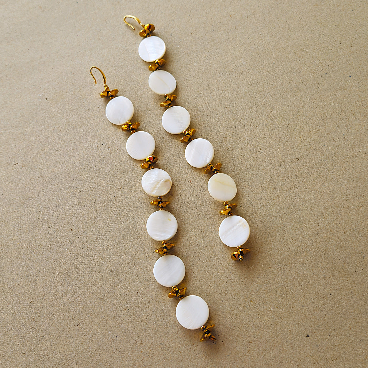 A pair of long dangling earrings with mother of pearl shells beads and gold toned cut glass beads
